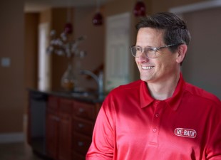 A close-up of a middle-aged man with glasses wearing a branded Re-Bath polo shirt. | Re-Bath