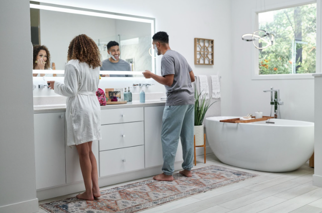 Couple getting ready in a bright, modern bathroom with a double vanity and freestanding tub. | Re-Bath
