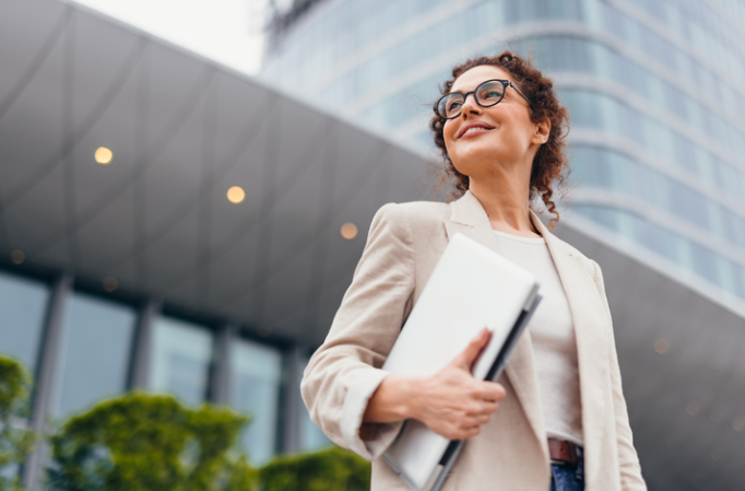 A professional woman holding a folder stands outside a modern office building. | Re-Bath