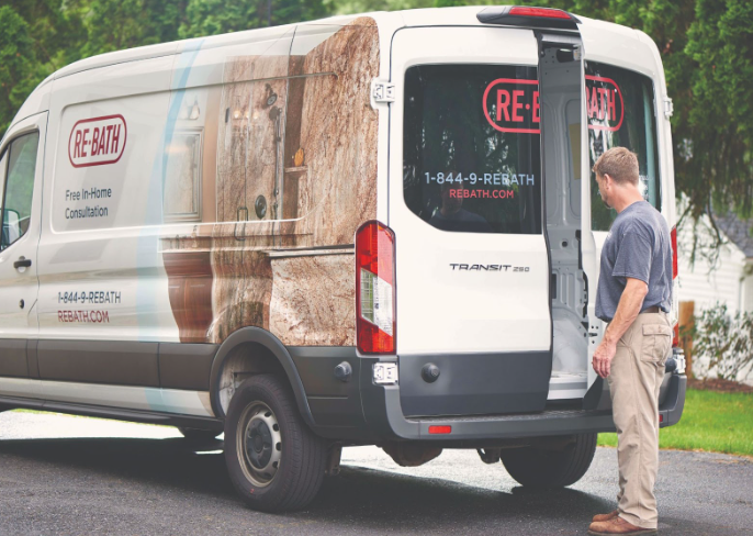 A Re-Bath service van parked on a residential street with its rear doors open and a worker standing beside it.
